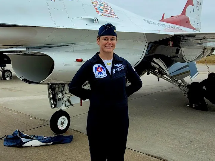 Major Lauren Schlichting stands in uniform with hands behind her back in front of a Thunderbird fighter jet.