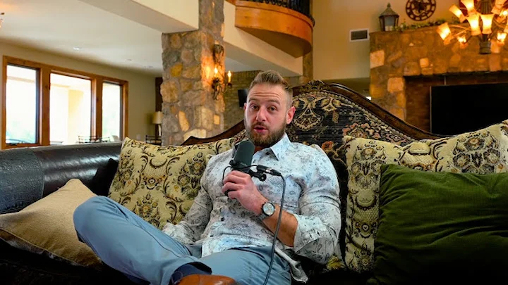 Casey Zander speaks into a microphone while sitting on a couch, sharing insights in a cozy home setting