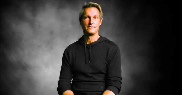 Mark Laita sitting in a black hoodie against a dark, smoky studio background.