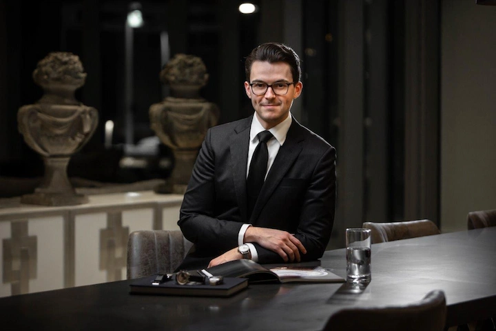 Teddy Baldassarre in a black suit seated at a table, representing his 2025 net worth and business success